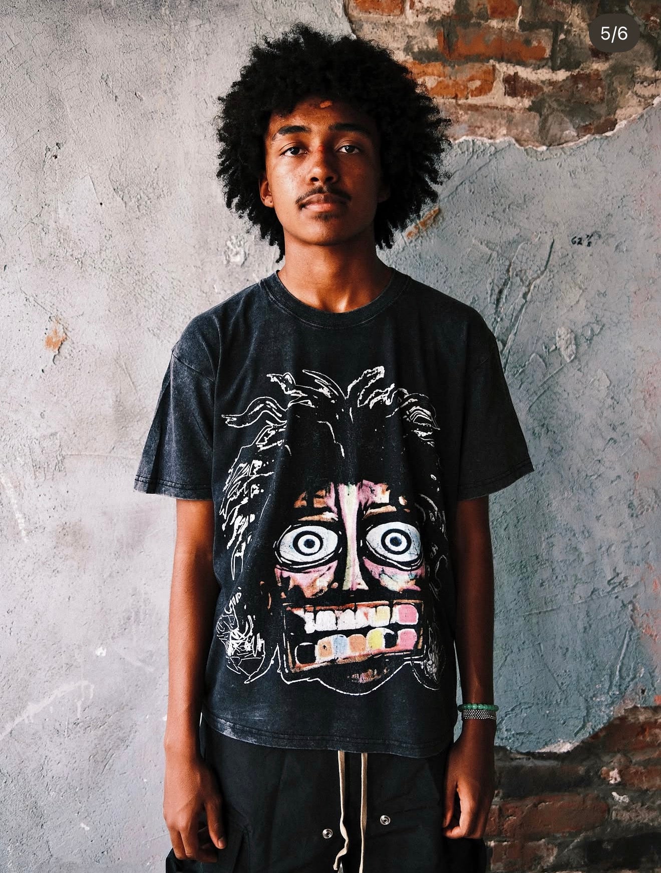 Model wearing the Pushin Flowers Crash Out tee in Acid Washed Black, front view showing the distressed chest graphic